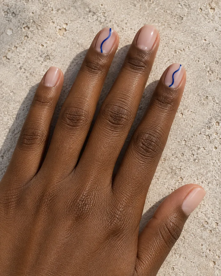 Uñas nude con líneas onduladas azules en dos uñas.